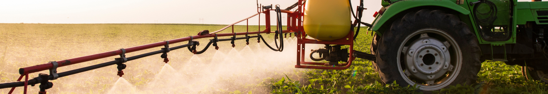 green tractor spraying field of crops